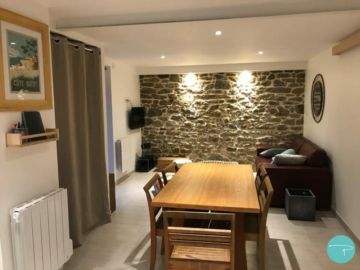 Photo projet finalisé appartement pour location, salon avec mur pierres, canapé cuir rouge et pouf tissu berbère