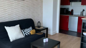 Photo pièce de vie, salon, salle à manger, noir, blanc et beige pour une location avec table à manger blanche, chaise métal blanche, chaise plastique noir, meuble TV métal blanc et bois, tapis marron et table basse métal noir et bois