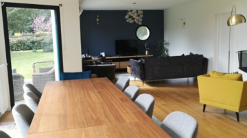 Photo pièce de vie colorée et moderne avec canapé velours gris, fauteuil jaune, chaises bleu, chaises grises, tapis multicolores, table à manger bois, meuble TV bois