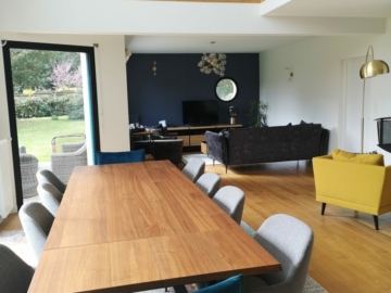 Photo pièce de vie colorée et moderne avec canapé velours gris, fauteuil jaune, chaises bleu, chaises grises, tapis multicolores, table à manger bois, meuble TV bois