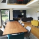 Photo pièce de vie colorée et moderne avec canapé velours gris, fauteuil jaune, chaises bleu, chaises grises, tapis multicolores, table à manger bois, meuble TV bois