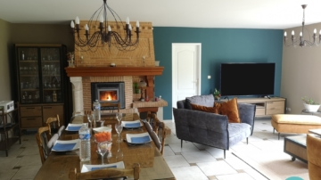 Photo d'un salon et d'une salle à manger avec une table à manger style campagne, canapé velours ocre, fauteuil velours gris anthracite et papier peint bleu canard