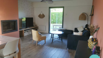 Photo d'un salon avec cheminée moderne terracotta, papier peint végétal blanc et or, lampadaire en fibre naturelle et canapé velours noir et suspension filaire métal noir