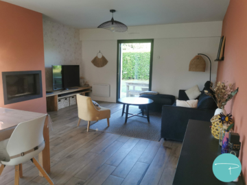 Photo d'un salon avec cheminée moderne terracotta, papier peint végétal blanc et or, lampadaire en fibre naturelle et canapé velours noir et suspension filaire métal noir