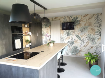 Rénovation d'une maison avec salon et salle à manger mur bleu vert, cuisine style industriel et papier peint panoramique feuillage, chambre beige et vert avec papier peint végétal, WC vert avec papier peint effet tasseaux bois, luminaires métal noir industriel grillage