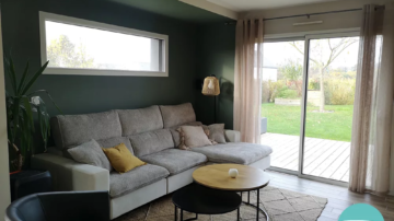 Salon, salle à manger et entrée à la décoration au style bohème chaleureux, cosy et coloré avec papier peint naturel vert, terracotta et jaune ocre. Murs vert dans salon et jaune ocre dans l'entrée. Mobilier en bois, suspension et lampadaire en fibre naturelle et chaises velours noir et vert