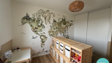 Chambre d’enfant décorée à Vitré autour d’une mappemonde panoramique illustrée. Une ambiance douce, naturelle et ludique, avec du mobilier en bois clair, des rangements pratiques et un univers inspiré du voyage, pensé pour stimuler l’imaginaire tout en conservant une pièce lumineuse et évolutive.